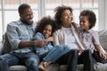 Happy mixed race couple parents relaxing on sofa with children.