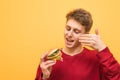 Happy boy with burger in his hands inhales the smell of fresh fast food and smiles on a yellow background. Young man sniffs an Royalty Free Stock Photo