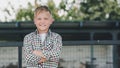 happy boy in checkered shirt standing with crossed arms and smiling at camera