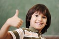 Happy boy in classroom with thumb up: green board