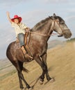 Happy boy in cowboy hat riding horse outdoors