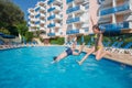 Happy boy and girl jump in blue pool near hotel at Royalty Free Stock Photo