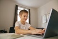 Small happy boy having online video lesson at laptop sitting at the table in his room. E-learning Royalty Free Stock Photo