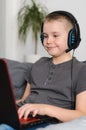 Happy boy in headphones playing online video game on laptop computer at home. Child sitting and use pc Royalty Free Stock Photo