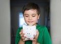 Happy boy holding piggy bank with smiling face. Close up portrait of a cheerful child showing money saving box. School kid Royalty Free Stock Photo