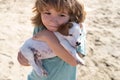 Happy boy hugging his dog against sand. Kid lovingly embraces his pet dog. Royalty Free Stock Photo