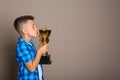 Happy boy kissing golden winning cup on beige background Royalty Free Stock Photo