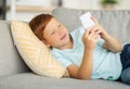 Happy boy laying on couch, using smartphone Royalty Free Stock Photo