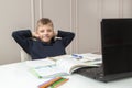 happy boy leans back in chair and puts hands behind head, sitting at table with notebooks, textbooks and pencils in front of