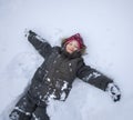 Happy boy lying on snow and making snow angel figure with hands and legs