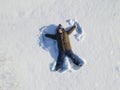 Happy boy lying on snow and making snow angel figure with hands and legs