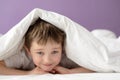 Happy boy playing in bed under a white blanket or coverlet Royalty Free Stock Photo