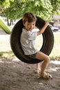 Happy Boy playing on a Swing wheel in the garden. Sunny summer day. activity for kids. child having fun and swinging on car tire Royalty Free Stock Photo