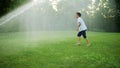 Happy boy playing with water sprinkler in field. Positive guy jumping in air Royalty Free Stock Photo