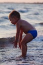 A happy boy is playing in the waves on the beach. Cheerful boy bathes in the sea waves at sunset Royalty Free Stock Photo