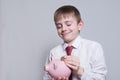 Happy boy puts a coin in a pink piggy bank. Business concept. Light background Royalty Free Stock Photo