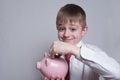 Happy boy puts a coin in a pink piggy bank. Business concept. Light background Royalty Free Stock Photo