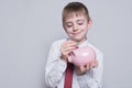 Happy boy puts a coin in a pink piggy bank. Business concept. Light background Royalty Free Stock Photo