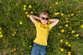 Happy boy puts his hands behind his head. Blond child lies on grass in dandelions field and dreaming. Top view Royalty Free Stock Photo