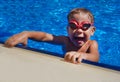 Happy boy with red goggles in open air swimming pool. Portrait of young boy leaning on edge of swimming pool on summer