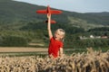 Happy boy in red T-shirt plays with toy plane in wheat field on mountains background. Flights and travel with children Royalty Free Stock Photo