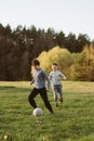 Happy boy running behind concentrated teenager who dribbling ball in game of football, friends playing soccer on field.