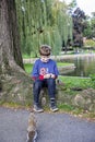 Happy boy sitting by lake in Boston public garden with squirrel Royalty Free Stock Photo