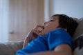 Happy boy sitting on sofa bitting finger nails while watching cartoon on TV. Mixed race Child resting in living room with bright