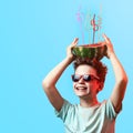 A happy boy in sunglasses holding watermelon with cocktail tubes on head on blue background Royalty Free Stock Photo