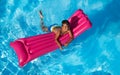 Happy boy swimming on pink inflatable mattress