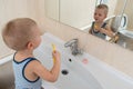 Happy boy taking bath in kitchen sink. Child playing with foam and soap bubbles in sunny bathroom with window. Little baby bathing