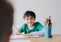 Happy boy using pencil drawing or sketching on paper, Cute kid with smiling face siting on table doing homework, Child enjoy art