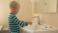 Happy boy washes his hands with soap and brushes his teeth in bathroom. Child loves water and hygiene procedures. Water activities