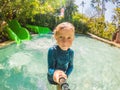 Happy boy on water slide in a swimming pool having fun during summer vacation in a beautiful tropical resort Royalty Free Stock Photo