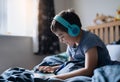 Happy boy wear wireless headphone listening music while sitting in bed, Cute young kid playing game on tablet,Positive child in Royalty Free Stock Photo