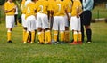 Happy boys in yellow shirts in sports team huddling with young coach