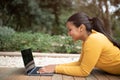 Happy brazilian college student girl preparing for exams or doing homework on laptop, lying on bench in park, side view Royalty Free Stock Photo