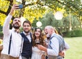 Bride, groom and guests with smartphone taking selfie outside at wedding reception. Royalty Free Stock Photo