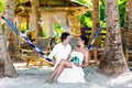 Happy bride and groom having fun in a hammock on a tropical beach under the palm trees. Summer vacation concept. Royalty Free Stock Photo