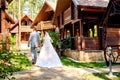 Happy bride and groom holding hands and walking near wooden house in park on wedding day, copy space. Wedding couple in love Royalty Free Stock Photo