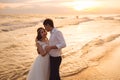 Happy bride and groom hugging on ocean beach at sunset time. Romantic couple newlyweds on their wedding day. Royalty Free Stock Photo