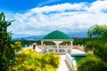 Happy bride and groom standing next to the stone gazebo amid beautiful tropical landscape. Sea, sky, flowering plants and palm tr