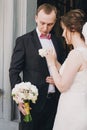 Happy Bride putting on stylish boutonniere on groom suit at doors after wedding ceremony in church. Happy stylish wedding couple Royalty Free Stock Photo