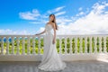 Happy bride standing next to the stone gazebo amid beautiful tropical landscape. Sea, sky, flowering plants and palm trees in Royalty Free Stock Photo