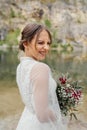 The happy bride in a white dress with a red bouquet on the bank of a river . Royalty Free Stock Photo