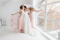 Happy bridesmaid hugging the bride covered by veil in the bedroom in the morning, having fun.