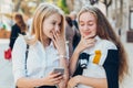 Happy bright positive moments of two stylish girls hugging and looking at the phone, discussing something on the street in the