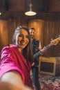 Happy brown-haired woman vocalist takes a selfie with male guitarist. Rock band practice before concert. Vertical indoor