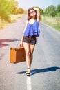 Happy Brunette beautiful girl traveler with suitcase on road, hitchhiking. Concept of travel, adventure, vacation, freedom. Waitin Royalty Free Stock Photo