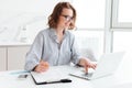 Happy brunette businesswoman in glasses using laptop computer while working in light apartment Royalty Free Stock Photo